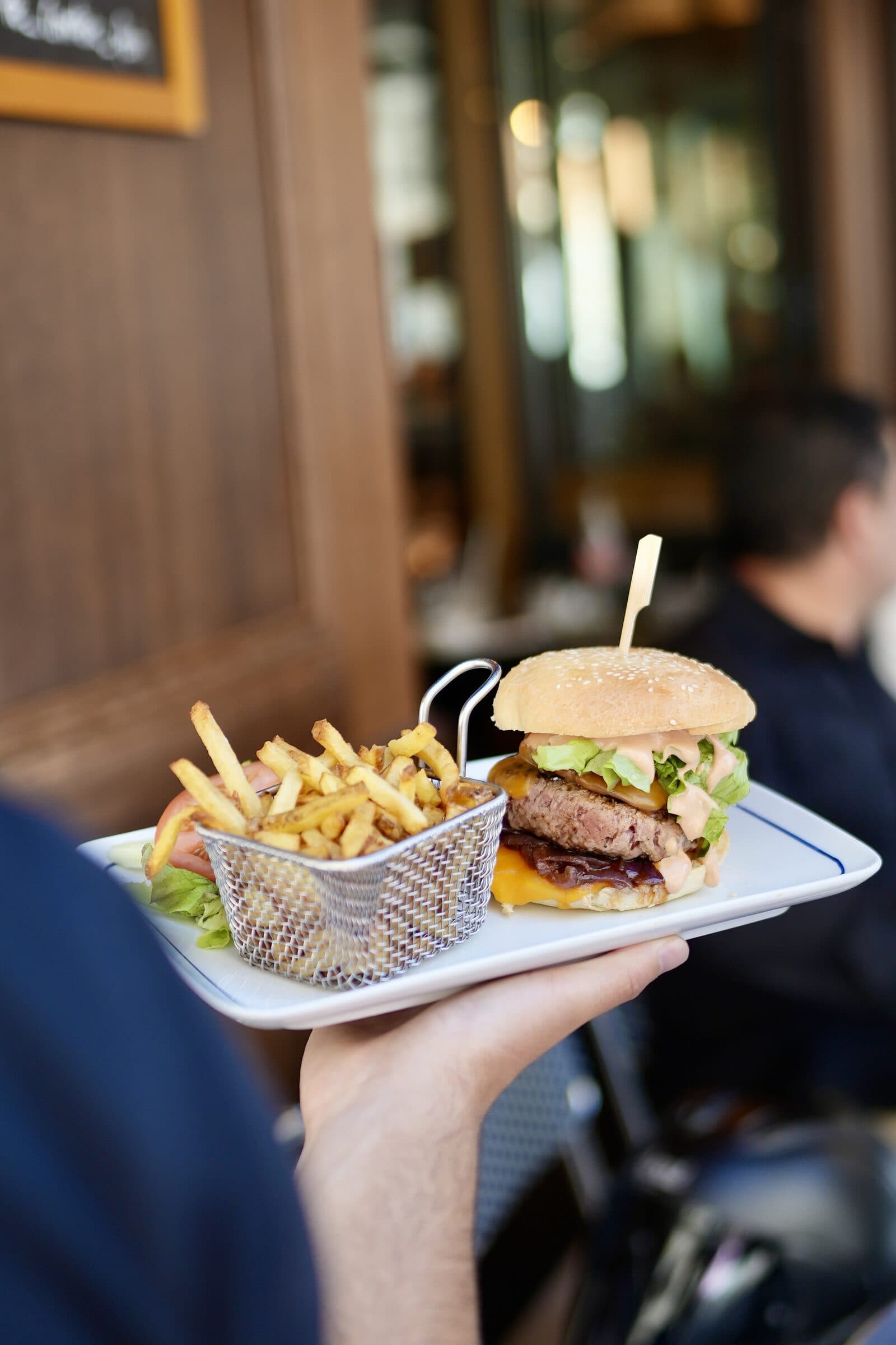 Burger maison et frites dorées en panier métallique, servis sur assiette Le Comptoir Foch par un serveur en salle