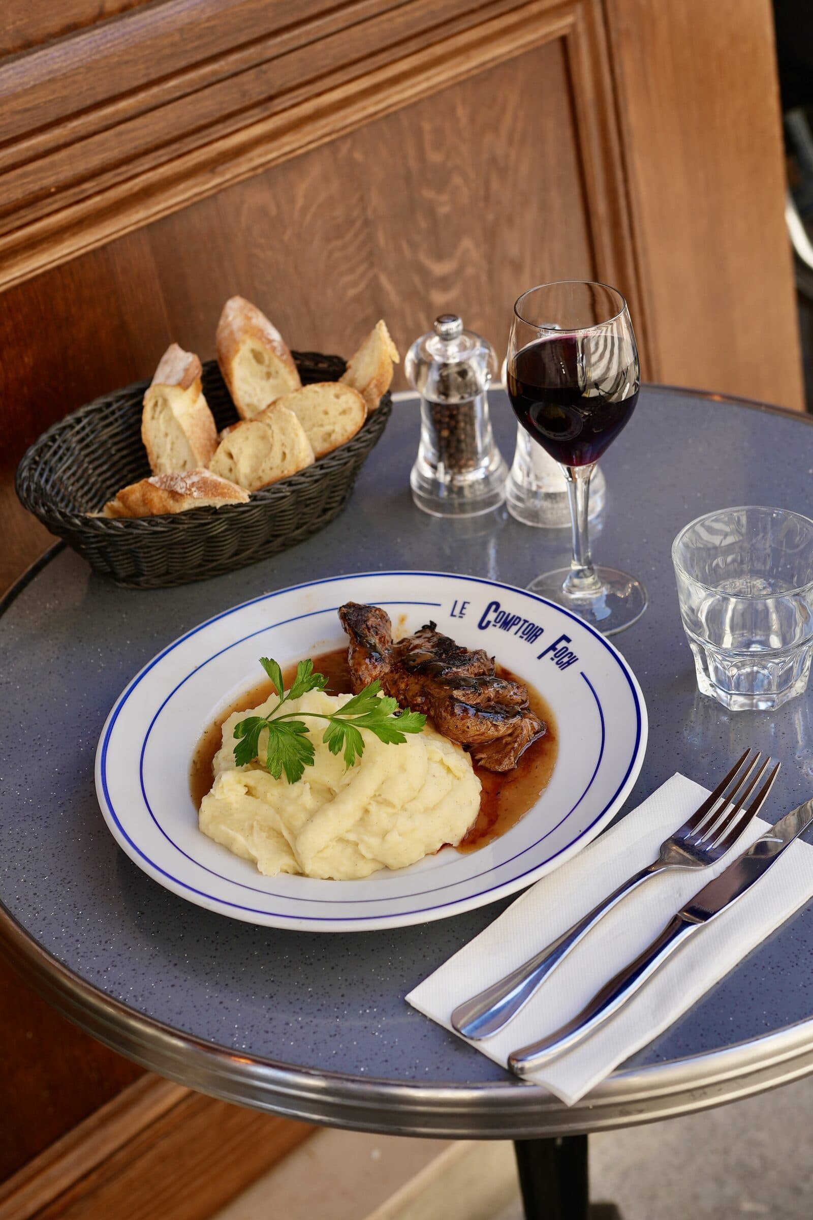 Côte d'agneau et purée maison sur assiette Le Comptoir Foch, verre de vin rouge et boiserie chaude en fond
