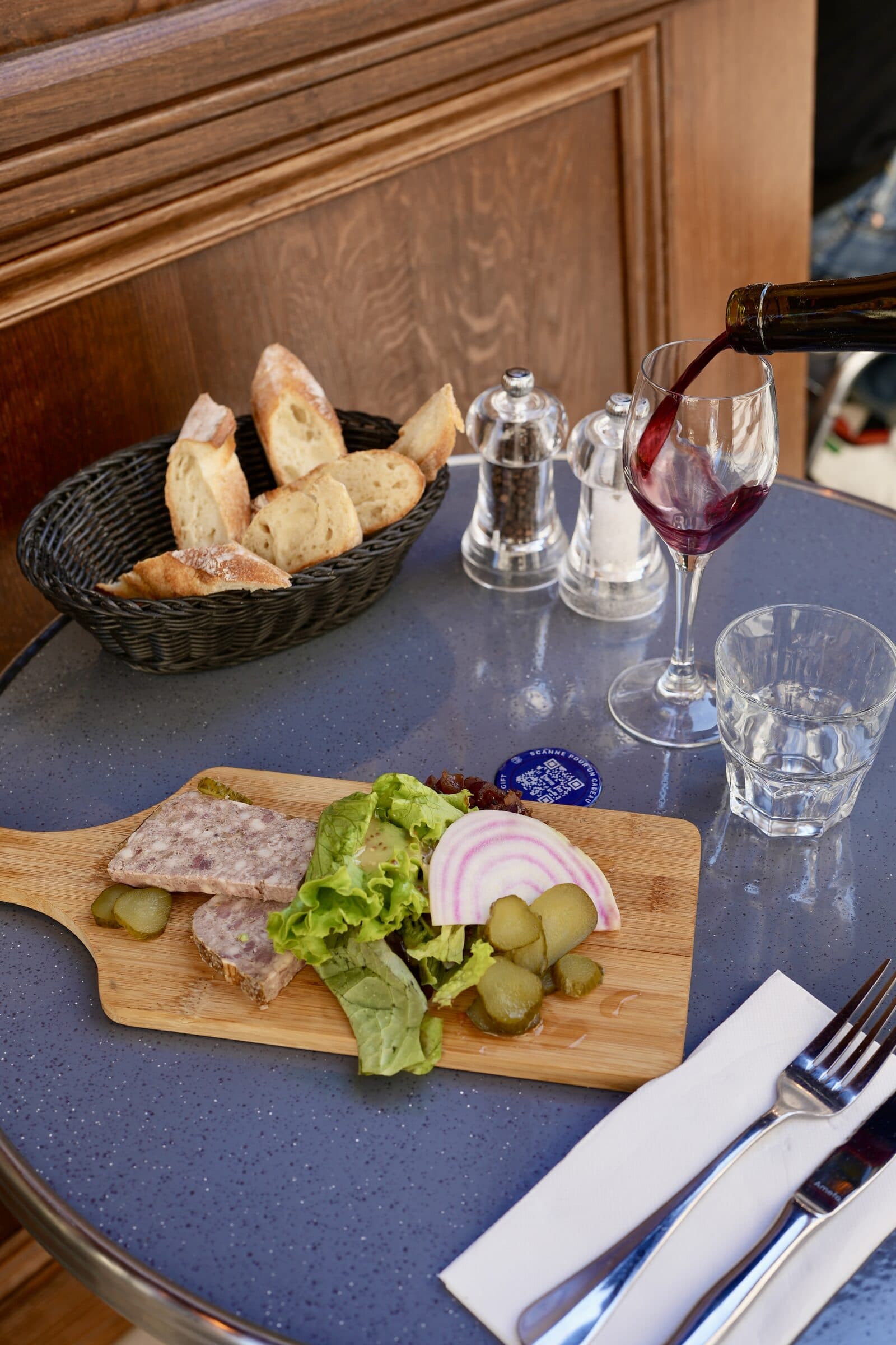 Planche de pâté de campagne avec cornichons et salade, vin rouge versé à la table du Comptoir Foch